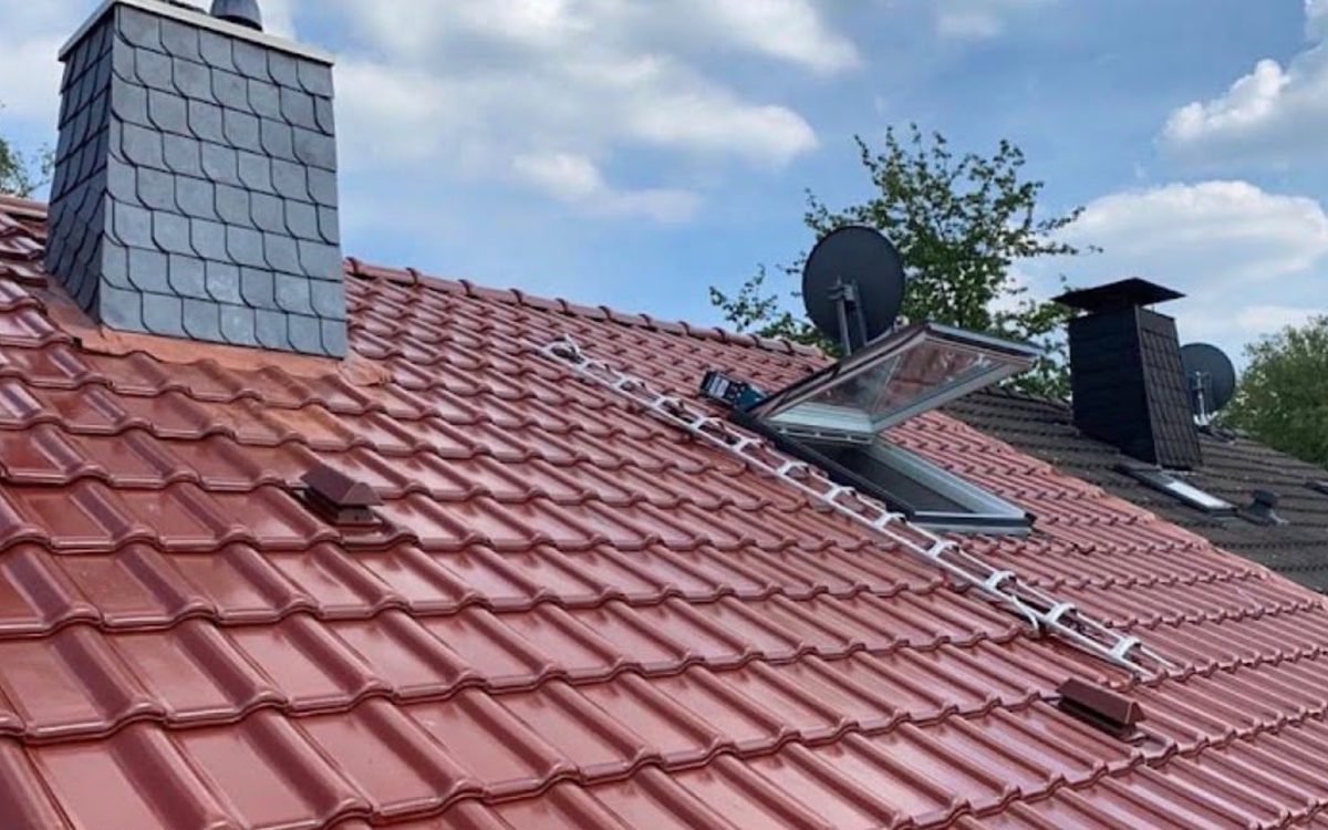Neues Velux-Dachfenster in rotem Ziegeldach neben einem schiefergedeckten Schornstein