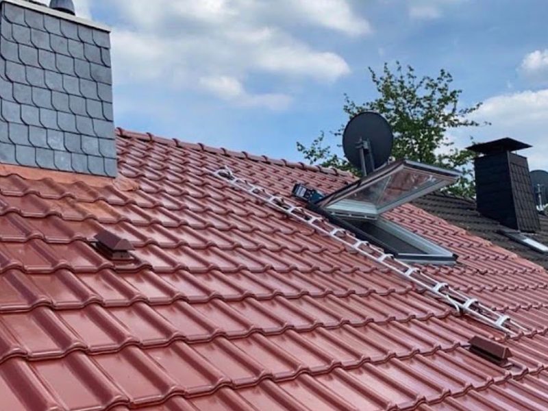 Rotes Ziegeldach mit neu eingebautem Velux-Dachfenster und schiefergedecktem Schornstein